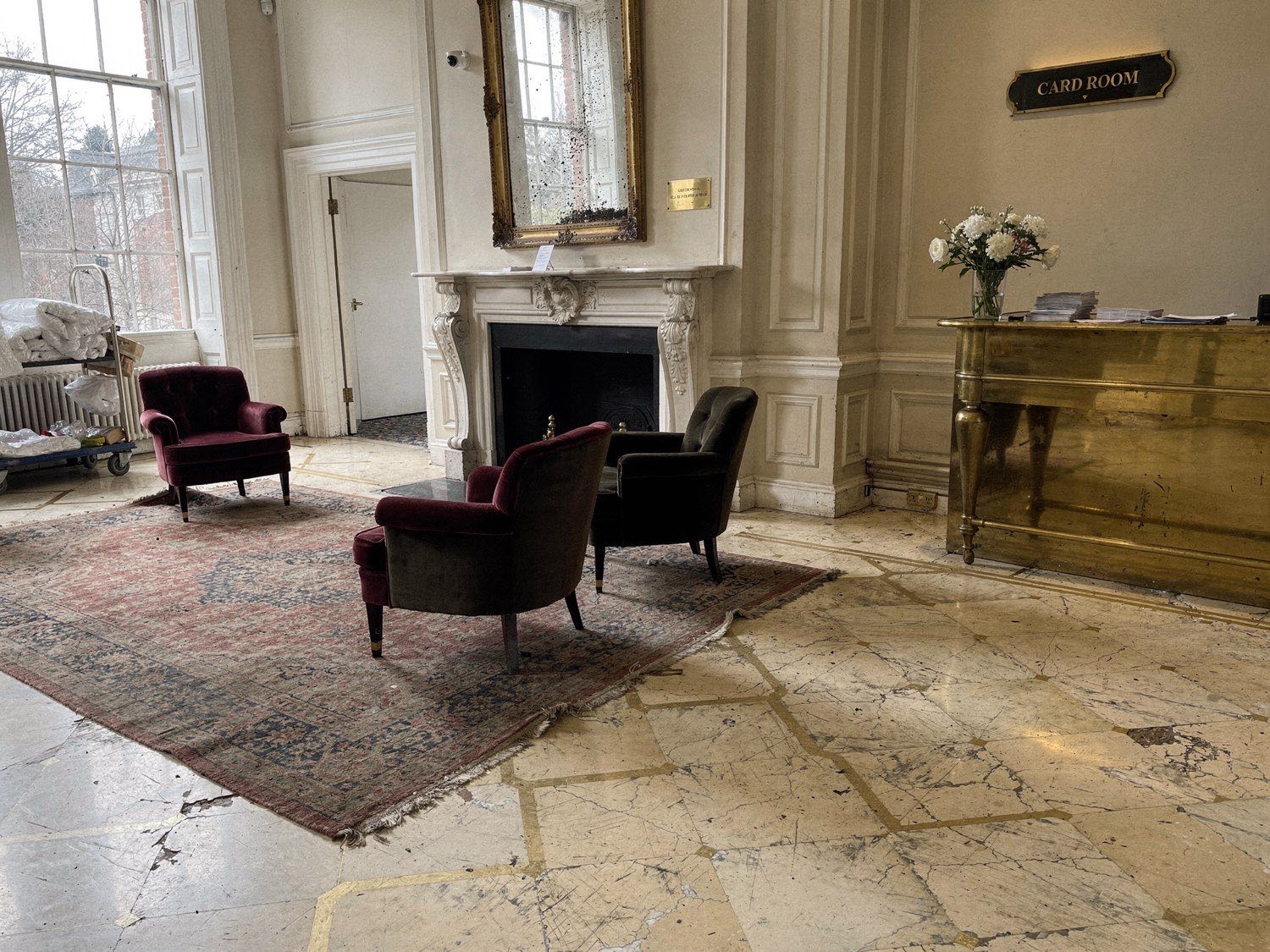 The Ivory Palace arrival lobby — marble fireplace, sash windows, faded rug